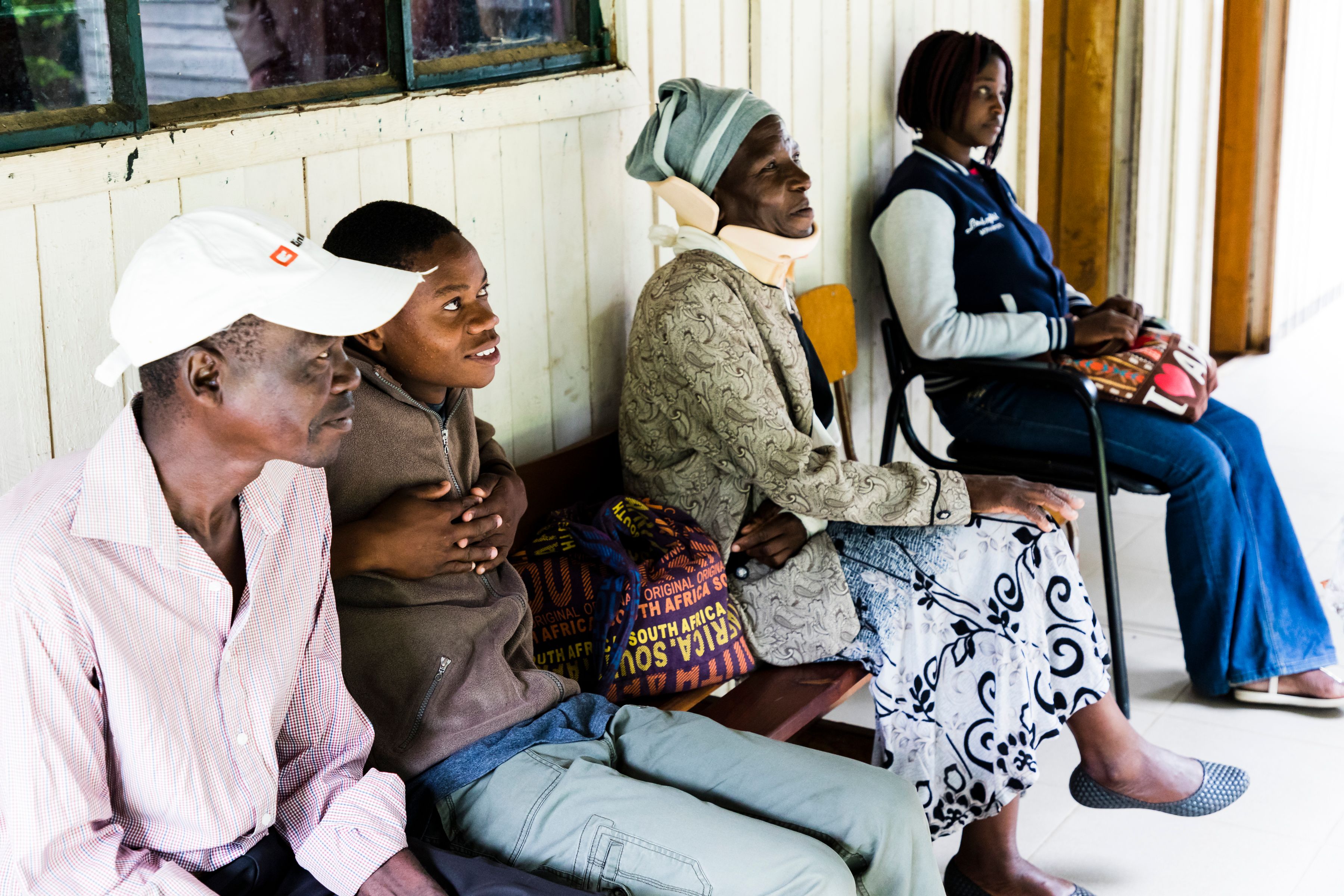 A man, a boy, an older woman and a young woman sitting on a bench and a chair while waiting